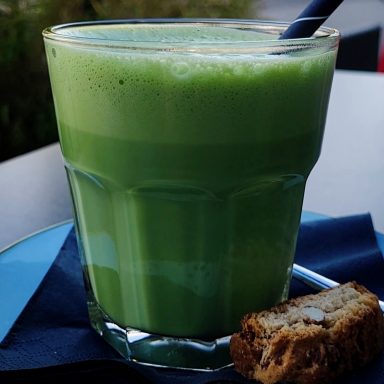 Ein Glas grüner Smoothie mit einem Strohhalm und einem Keks auf einem Unterteller.
