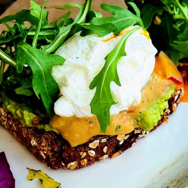 Avocado-Toast mit Rucola und einem pochierten Ei auf Vollkornbrot.